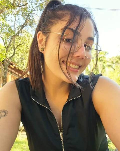 Larissa smiling outdoors, with glasses and her hair tied back.